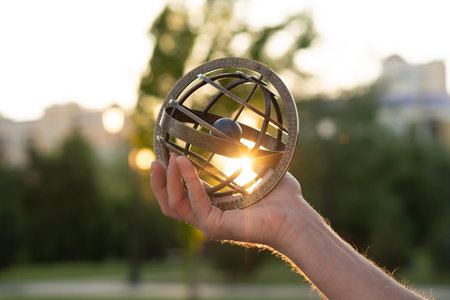 Extended arm holding antique globe illuminated by sunset rays. Armillary sphere astronomical...