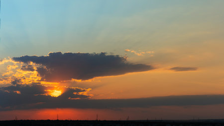 A scenic sunset with the sun hidden behind layered clouds, producing an intense orange glow in the...