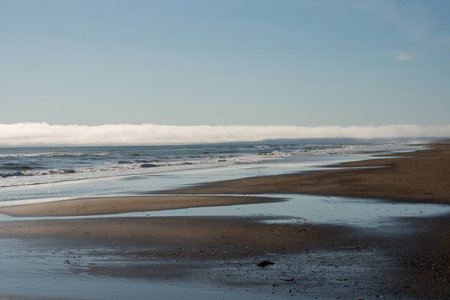 A sandy beach stretches into the distance with shallow pools reflecting the sky, while ocean waves...