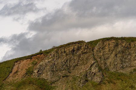 A weathered cliff with visible erosion and rocky surfaces is partially covered in vegetation, set...