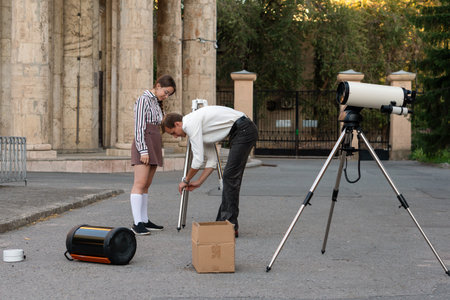 Instructor sets up the telescope tripod while a student watches closely during an outdoor astronomy...