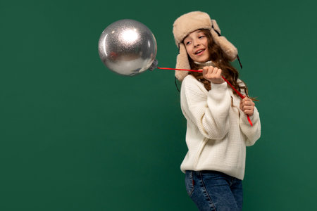 Playful girl swinging a large silver ornament on a red ribbon.の写真素材