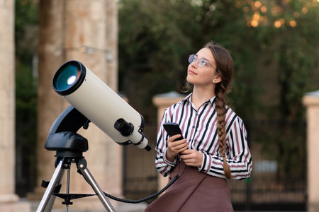 Girl with long braided hair and glasses looks upward with curiosity beside a mounted telescope near...