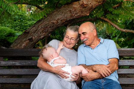 Senior couple sitting on a wooden garden bench, happily holding and interacting with their smiling...