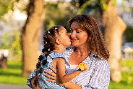 Close-up of a child giving her smiling mother a sweet kiss, both dressed in blue stripes and bathed in soft evening light.の写真素材