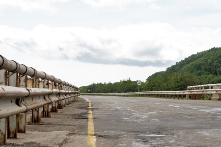 Rusting steel guardrail lines a country bridge road, guiding perspective toward forested hills...