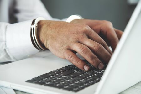 young man hand handcuffs on keyboard in office