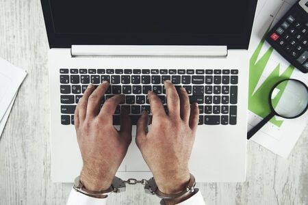 young man hand handcuffs on keyboard in officeの写真素材