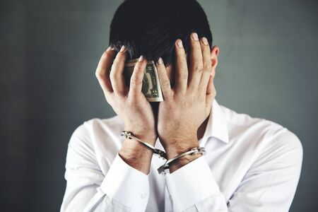sad man hand money with handcuffs on dark background