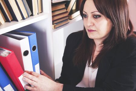 Businesswoman taking binders from a shelf at office