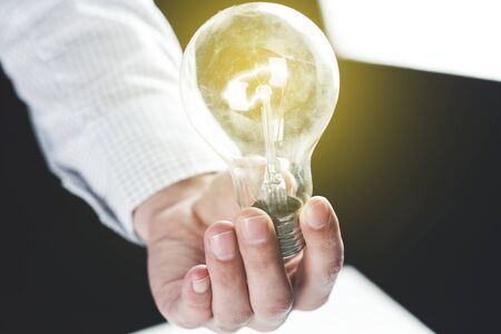 young man hand holding light bulb on dark background