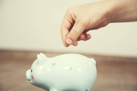 girl hand with blue  piggy bank on brown background