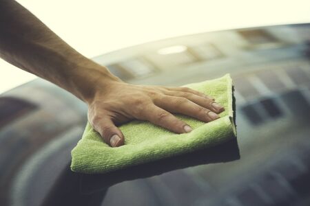young man cleaning blue car hood background