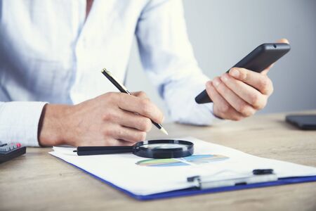 man hand phone with magnifier and graph on desk