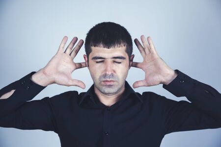 sad man hand in ear on gray wall background