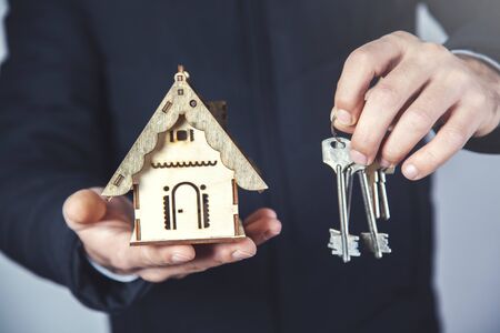 man hand holding wooden house model with keyの写真素材