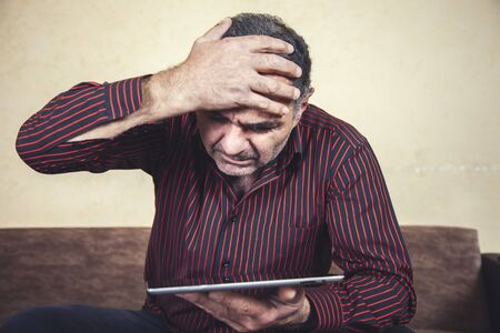 sad or angry man hand holding tablet sitting in sofaの写真素材