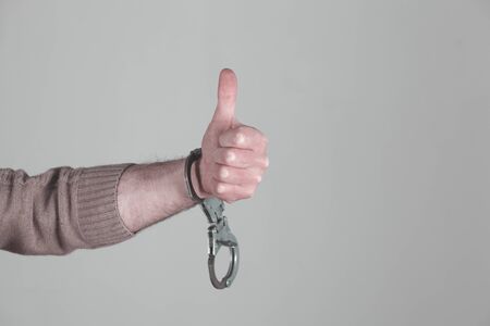 man hand handcuffs with okay sign on grey background