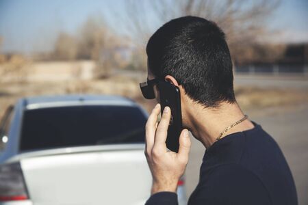 Young man holding a phone in his hands on a background of a car