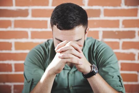sad man hand in face on brick wall background