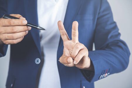 Young businessman showing victory sign with pen