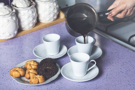 Woman hand pouring greek coffee from a copper pot on a white cup 