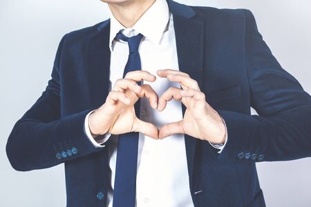 businessman shows heart on a gray background