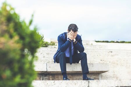 Young businessman is sitting in park after being firedの写真素材