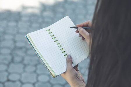 young girl hands with pen writing on notebook in park