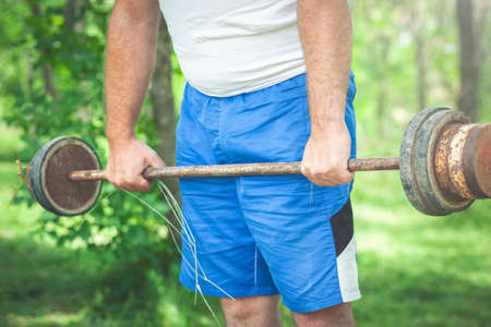 Sporty man in a white t-shirt and shorts pick up heavy barbell in natureの写真素材