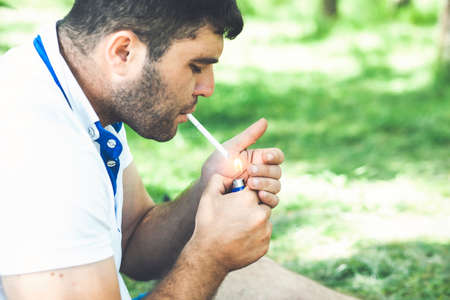hand of man holding a cigarette with green natural background