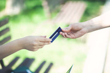 Close-up of transfer of credit card from males hand to that of female over green backgroundの写真素材