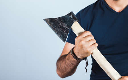 A man holds an ax in his hands against on gray background