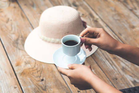 Woman's hand with a white cup of coffee with wooden background. The concept of a coffee break, a pleasant time of rest, enjoy the fresh coffeeの写真素材