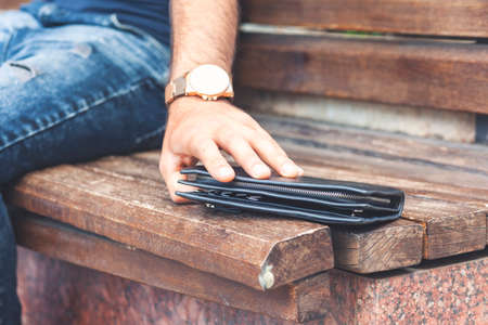 hand pulling a wallet forgotten on a wooden bench in a park.
