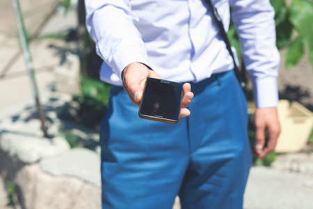 A young man holds a phone in his hands on the street. Businessman holds the phone in his hands on the streetの写真素材