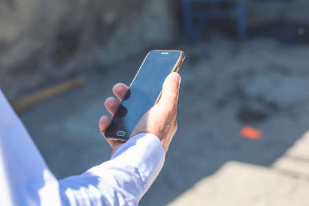 Man uses his Mobile Phone outdoor, close up. Image of a mans hands using a mobile smart phoneの写真素材