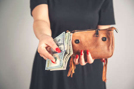 Young woman pulls out dollar banknotes money from brown wallet bagの写真素材