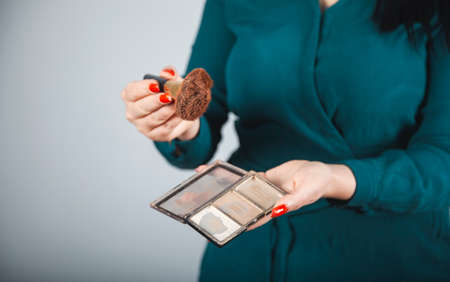 Beautiful young woman with makeup brushes and cosmetics on gray background.の写真素材