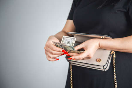Young woman pulls out dollar banknotes money from brown wallet bagの写真素材