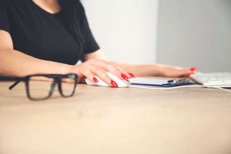 Side View of female hands using computer on table with glasses and other stuffの写真素材
