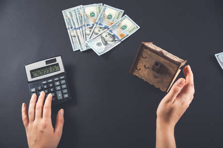 A woman holds in her hand a model of a house and money for real estate investment.の写真素材