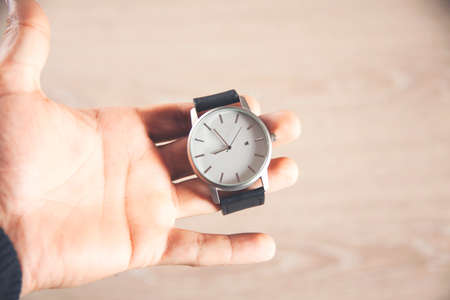 hand holds clock isolated on wooden background