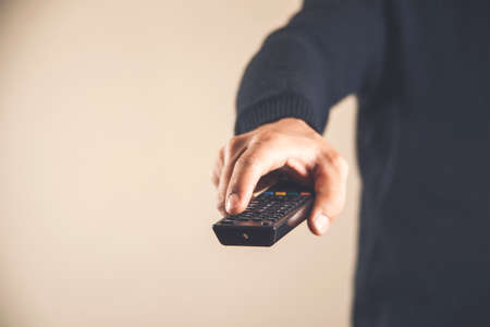 A man holds in his hand TV remote control. The man switches channels, choosing what to watch. Recreation and entertainment conceptの写真素材