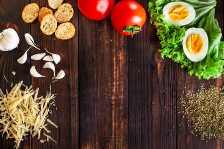 Empty space for text, food photography. Wooden brown background, spices, salt, cheese, eggs, salad, tomatoes, crackers, garlic.の写真素材