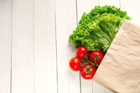 Paper bag on a wooden white background, vegetables from the store. Tomatoes, salad. Empty space for text.の写真素材