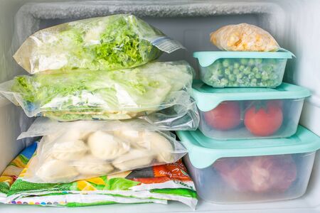 Frozen vegetables and meat in blue plastic containers. Frozen yellow corn, green peas, red tomatoes, meat, dumplings, vegetable mix, salad.の写真素材
