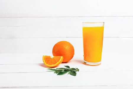 Orange juice in a tall glass. Cool drink on a white wooden background. Sliced orange in the background. Empty space for text.の写真素材