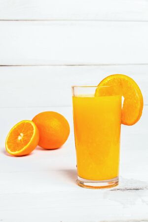 Orange juice in a tall glass. Cool drink on a white wooden background. Sliced orange in the background. Empty space for text.の写真素材