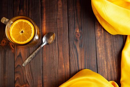 Tea with orange, metal spoon, yellow cloth, wooden brown background. Citrus drink in a transparent cup, empty space for text. Food composition.の写真素材